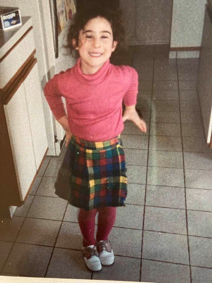 Childhood photo in a pink turtleneck and plaid skirt